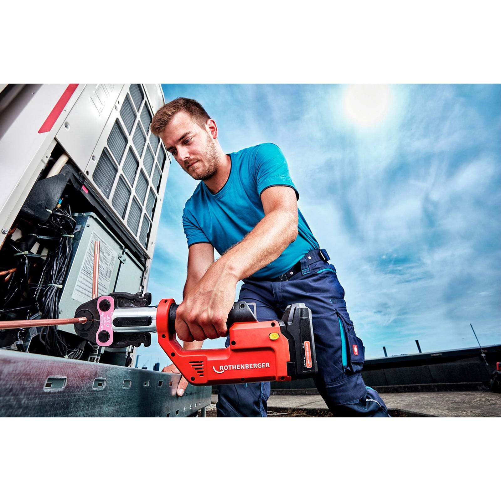 Ein Mann bedient ein rotes Rothenberger-Werkzeug an industrieller Ausrüstung unter einem blauen Himmel und trägt ein blaues Hemd und dunkle Hosen.