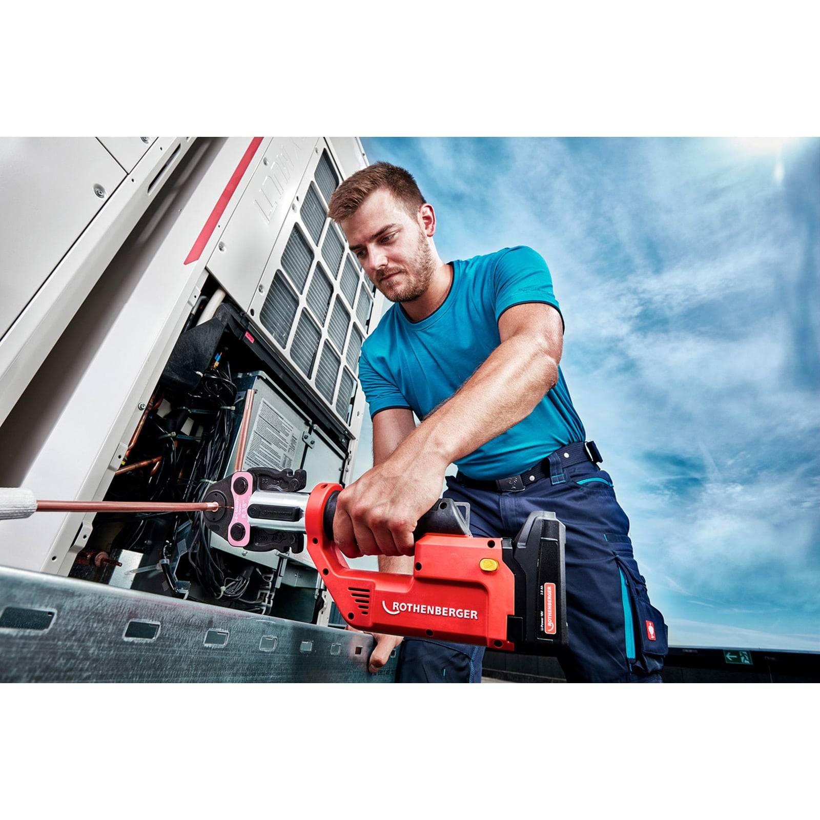 Eine Person in Arbeitskleidung bedient ein rotes Werkzeug an industrieller Ausrüstung im Freien. Der Himmel ist klar, was auf Tageszeit hindeutet.