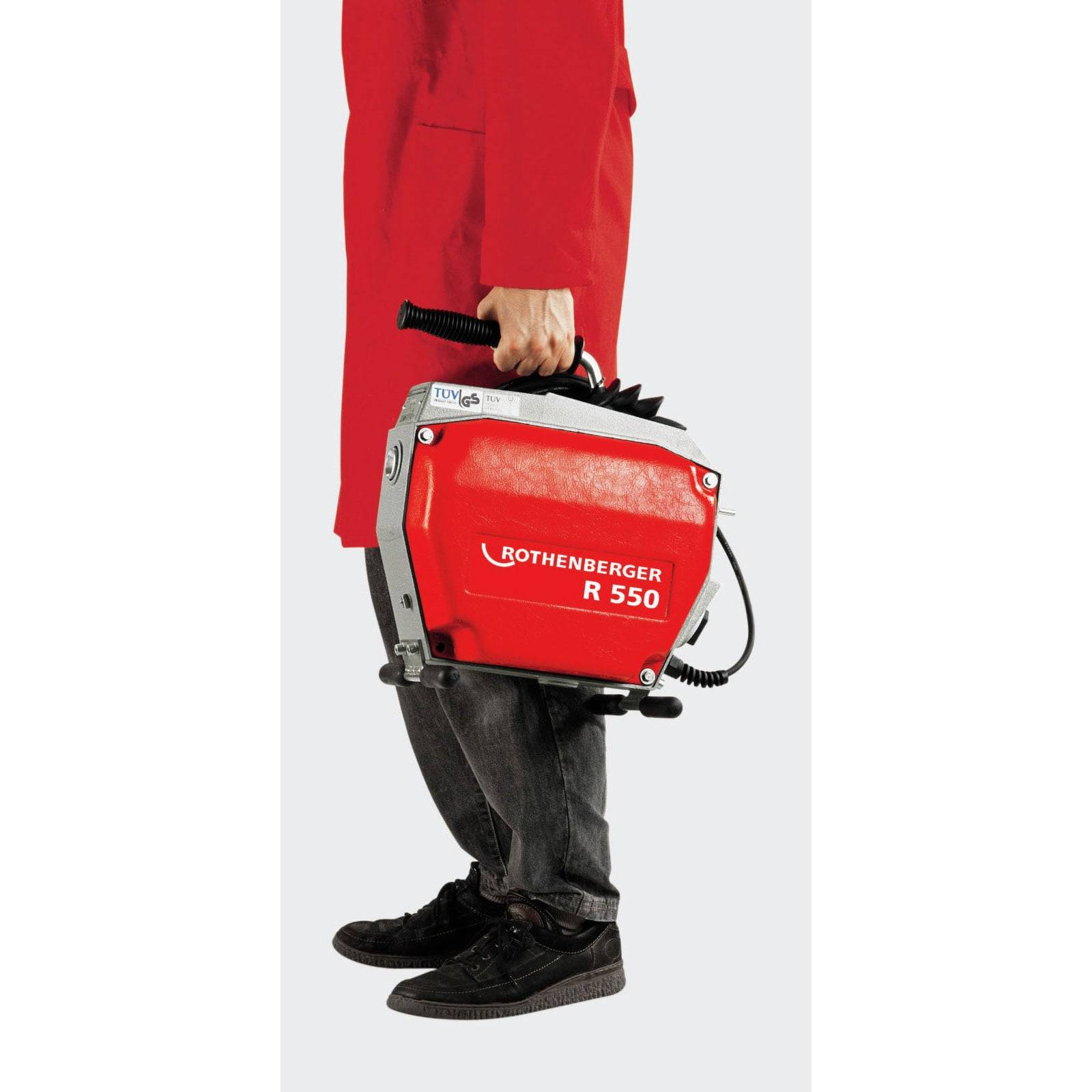 Eine Person in einem roten Mantel hält eine rote Rothenberger R 550 Rohrreinigungsmaschine, die vor einem einfarbigen Hintergrund präsentiert wird.