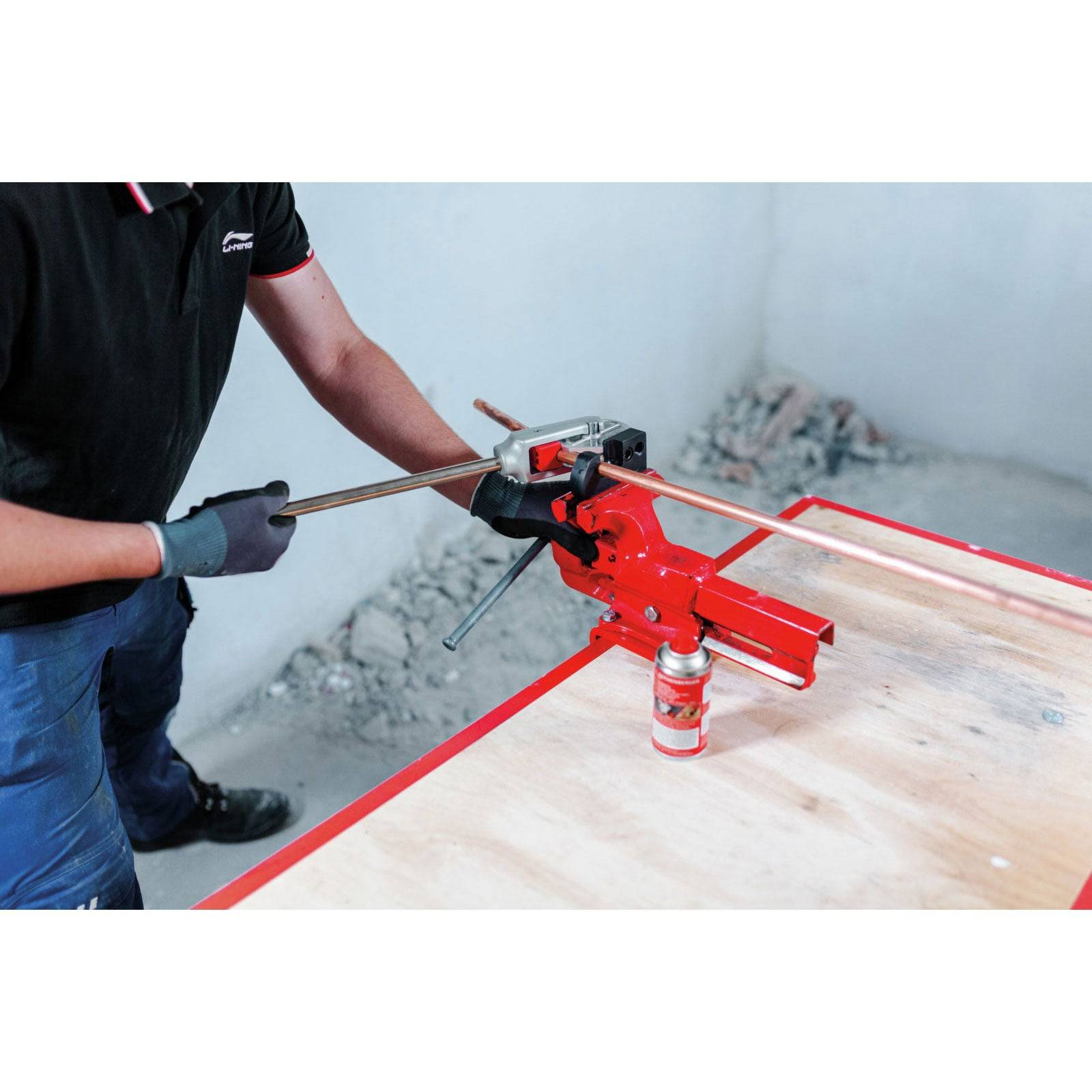 Eine Person, die einen Metallbieger auf einem Holztisch verwendet; eine Dose Schmiermittel ist unterhalb des Biegers sichtbar.