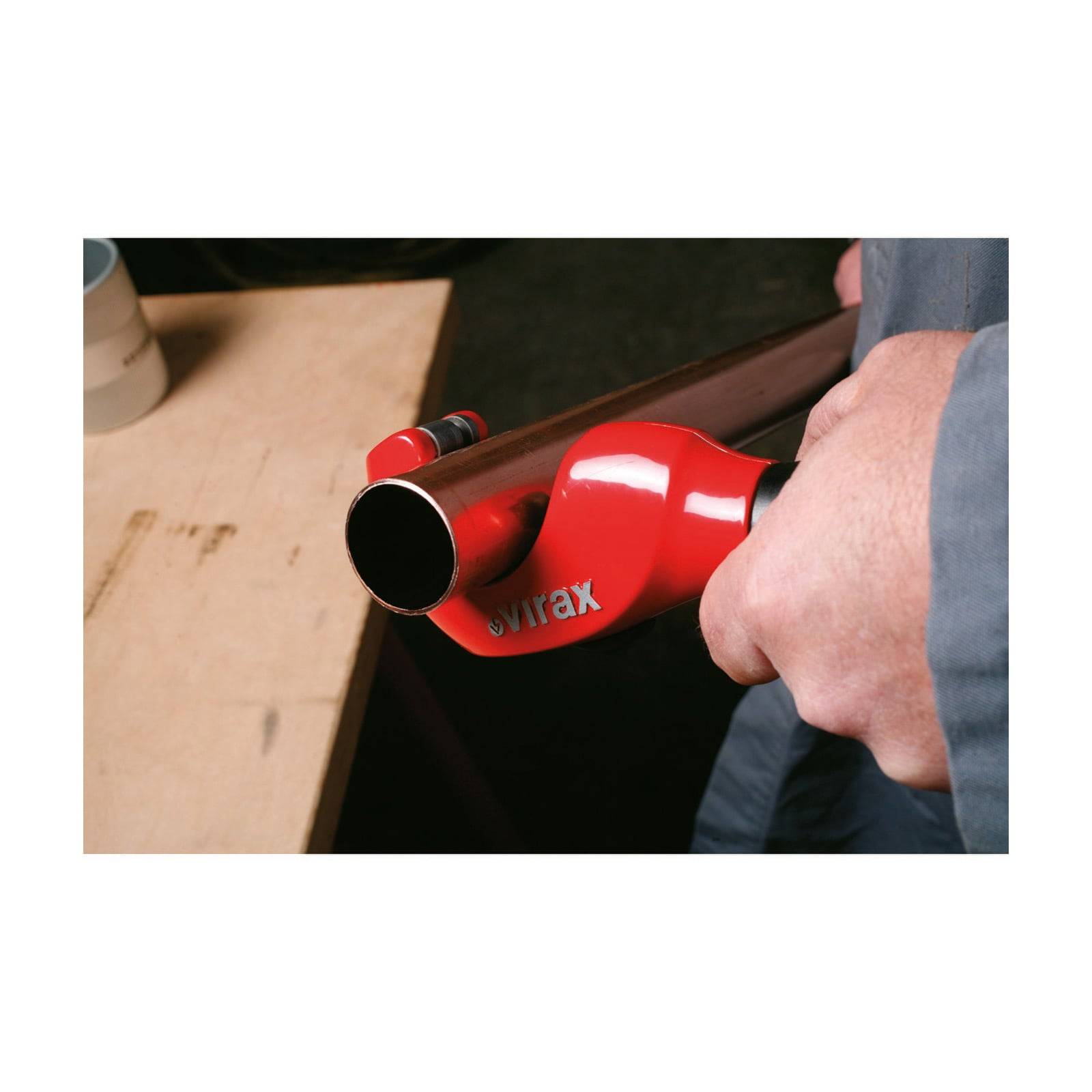 Eine Person verwendet ein rotes Swrax-Werkzeug, um ein Metallrohr zu biegen und demonstriert die Rohrbiegetechnik auf einem Holztisch.