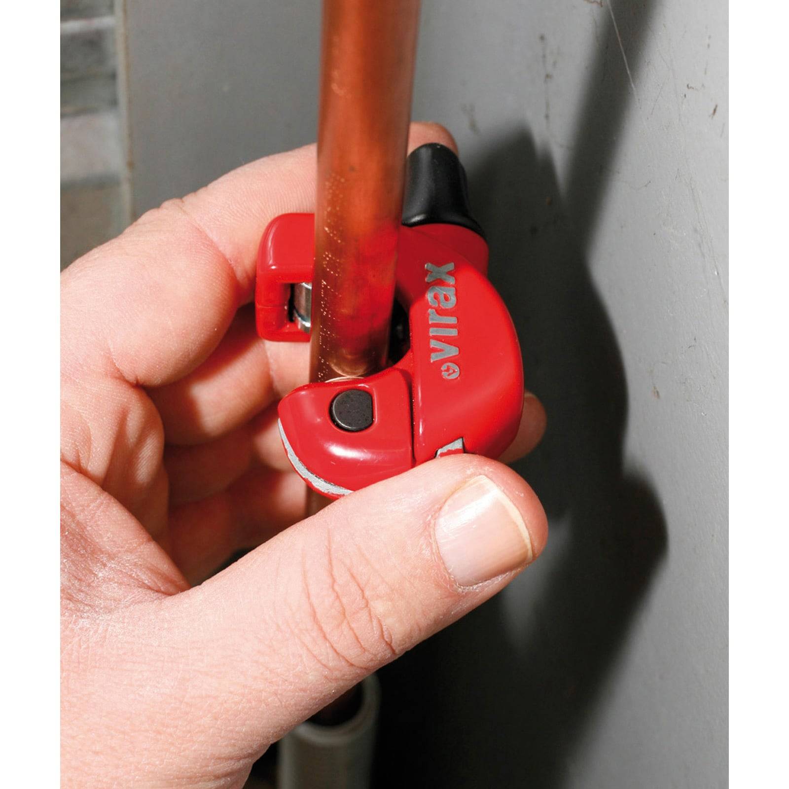 Eine Hand, die einen roten Rohrabschneider verwendet, um ein Kupferrohr zu schneiden, wobei der Markenname auf dem Werkzeug sichtbar ist.