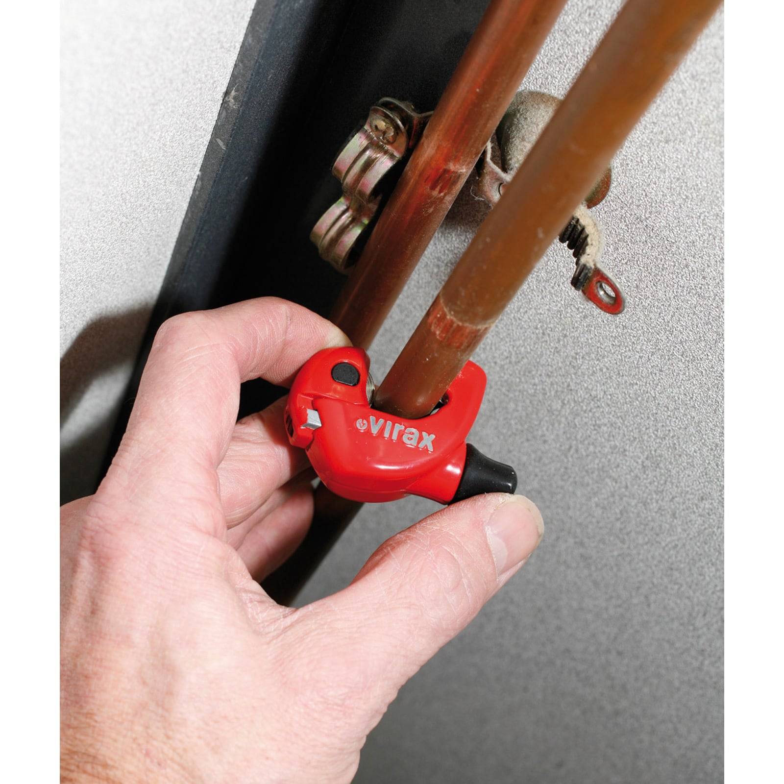 Eine Hand verwendet einen roten Rohrabschneider, um eine Kupferrohrleitung auf einer Metalloberfläche durchzuschneiden und zeigt dabei ein Klempnerwerkzeug in Aktion.