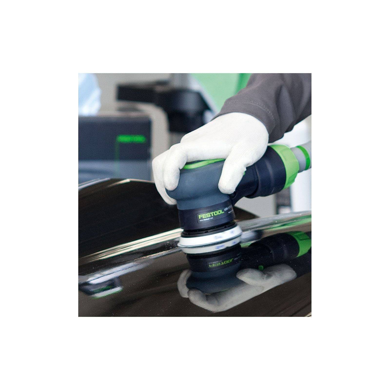 Eine Person verwendet einen tragbaren elektrischen Polierer auf einer schwarzen glänzenden Oberfläche und trägt weiße Handschuhe für Präzision und Sicherheit.