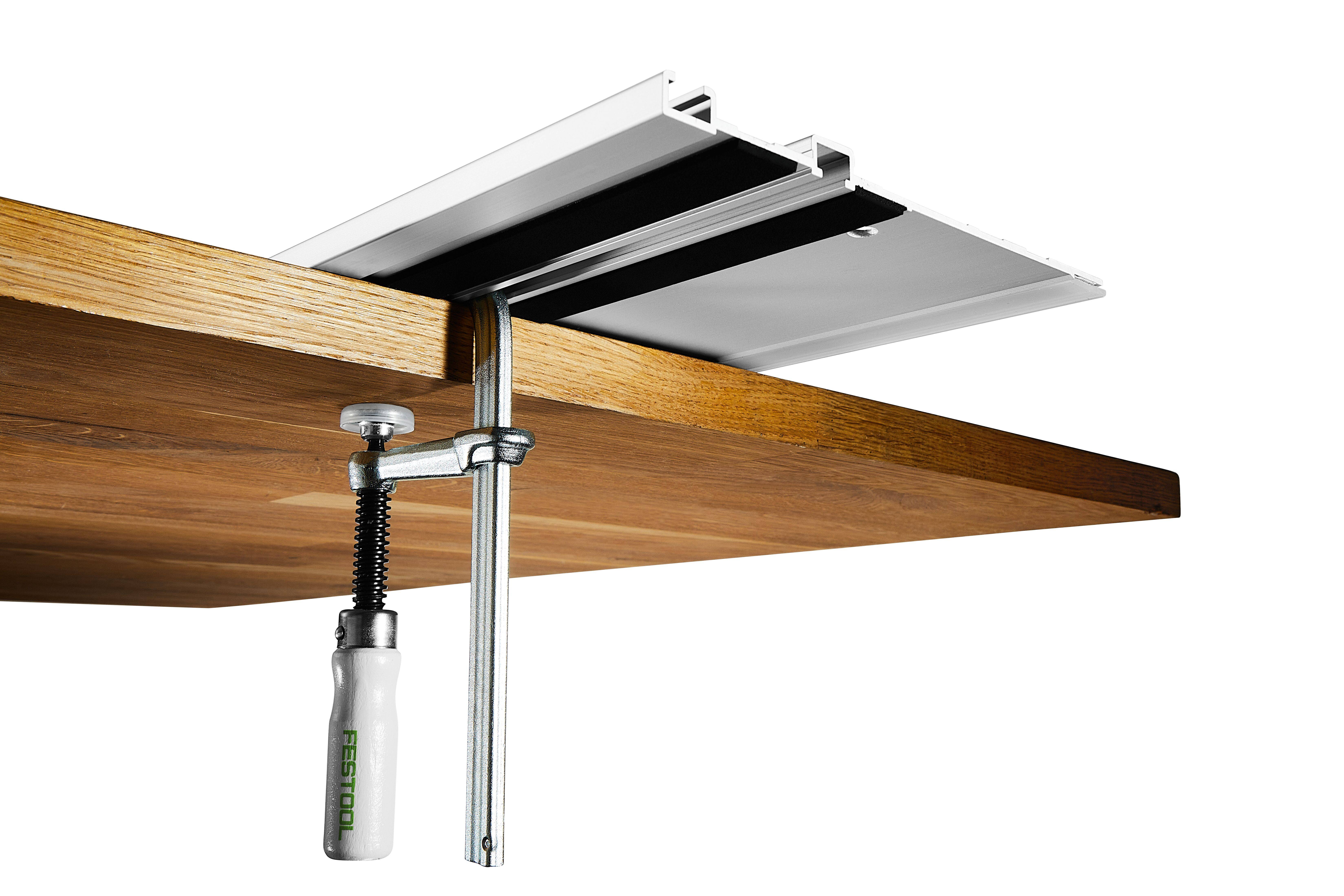 Unteransicht einer auf einer Tischplatte montierten Spannvorrichtung, die eine metallische Schiene oder ein metallisches Gleitschienensystem unter einem Holzschreibtisch sichert.