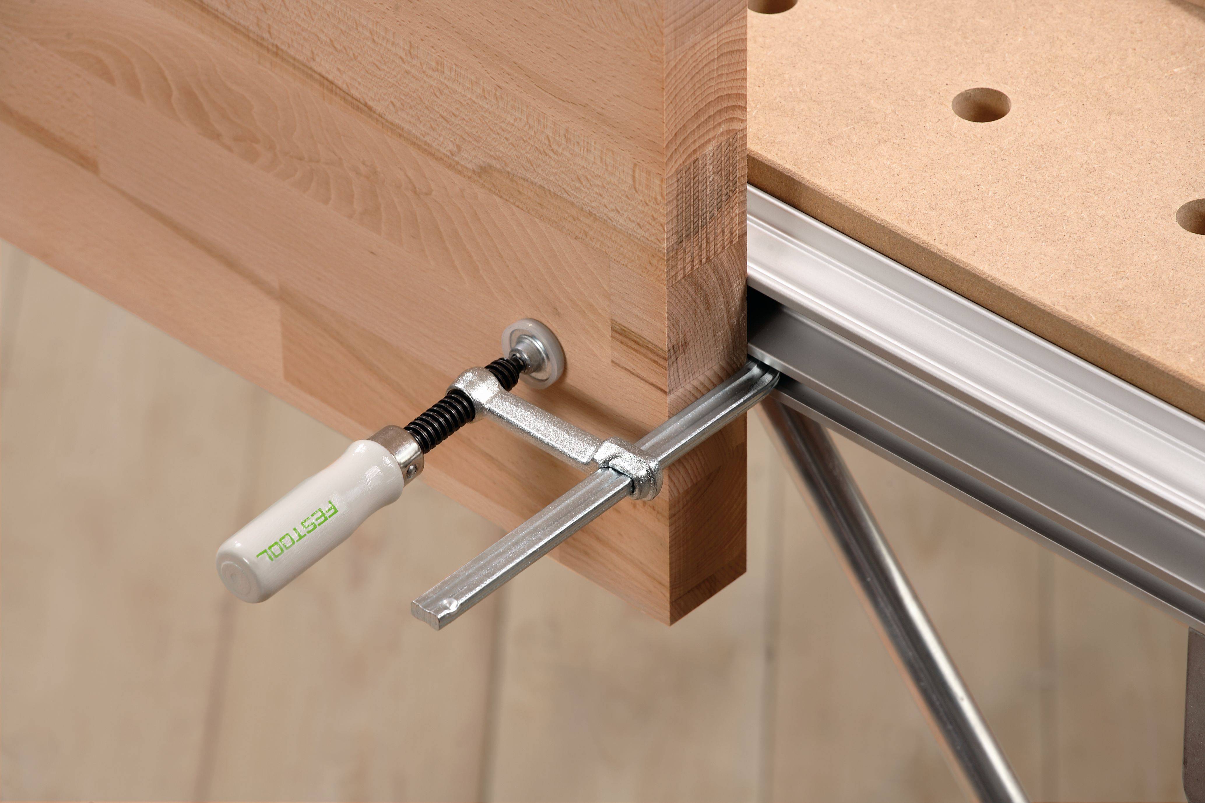 Nahaufnahme einer Holzbearbeitungszwinge, die ein Holzbrett auf einer Werkbank zum Schneiden oder Zusammenbau sichert.