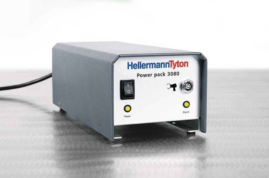 Ein graues HellermannTyton Power Pack 3080 Gerät mit einem Netzschalter, Netz- und Signalanzeigelampen sowie einer Anschlussschnittstelle auf seiner Frontplatte.