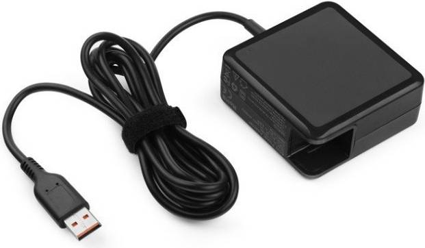 Ein schwarzes Laptop-Ladegerät mit aufgewickeltem Stromkabel und Stecker, neben einer kleinen, geöffneten Pappschachtel auf einer weißen Oberfläche platziert.