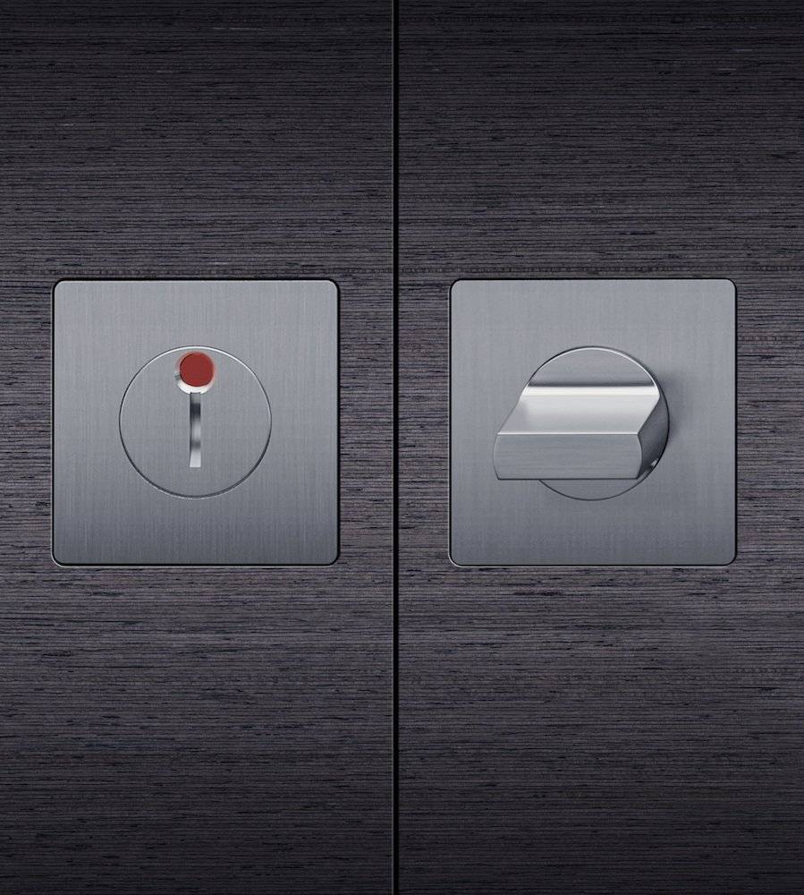 Nahaufnahme eines modernen, metallischen Türschlosses und Griffes auf einer dunklen Holzoberfläche mit minimalistischem Design.