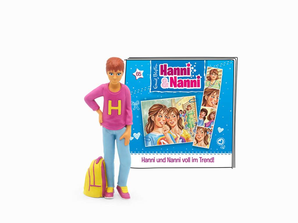 Eine Jungenpuppe mit gelbem Rucksack steht neben einem „Hanni & Nanni