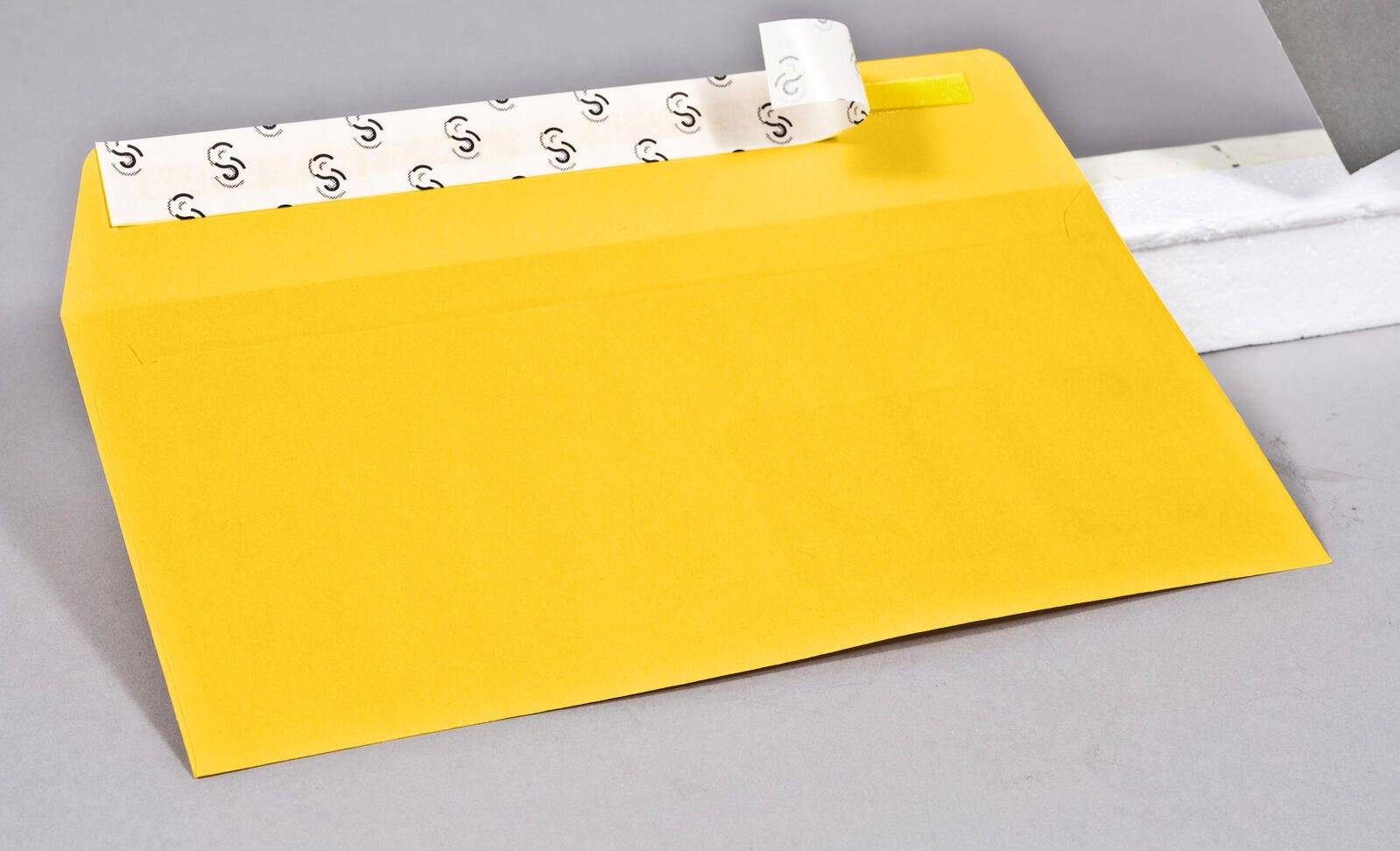 Ein gelber Umschlag mit einem Abzieh- und Verschlussstreifen, der teilweise geöffnet ist und das Klebemittel im Inneren zeigt.