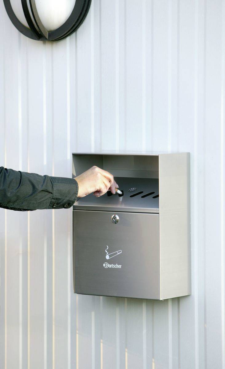 Person führt eine Zigarette in einen wandmontierten Aschenbecher aus Edelstahl an einer gewellten Metallwand ein.