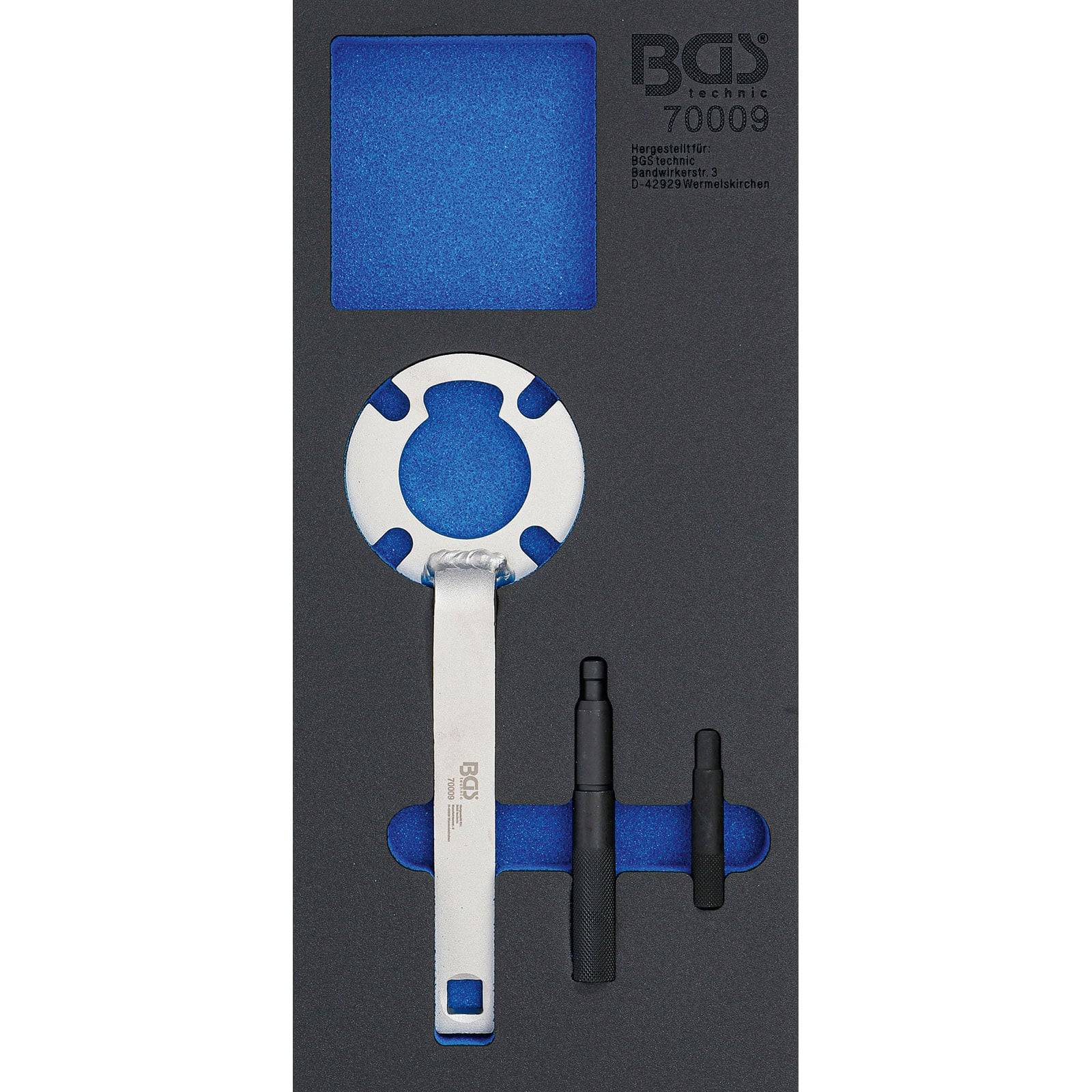 Ein Werkzeugsatz mit einem weiß-blauen Schraubenschlüssel, zwei schwarzen zylindrischen Werkzeugen und einem blauen Fach, gekennzeichnet mit 'BGS technic 70009'.