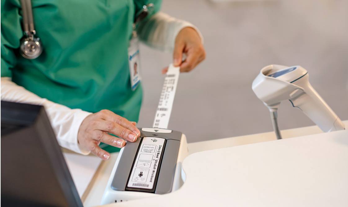 Gesundheitspflegekraft, die ein Patientenarmband an einem tragbaren Barcode-Lesegerät scannt, wahrscheinlich zur Identitäts- oder Medikamentenüberprüfung.