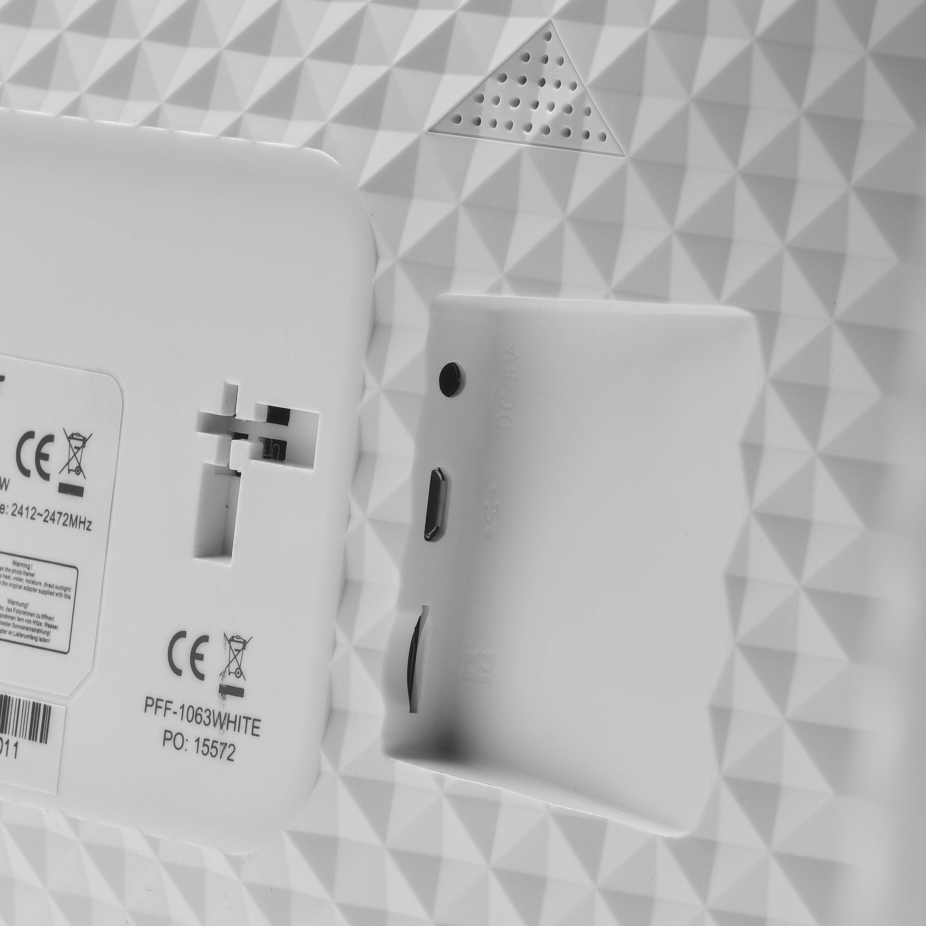 Nahaufnahme eines weißen elektronischen Geräts, das CE-Zertifizierungszeichen und verschiedene Anschlüsse auf einer strukturierten Oberfläche mit Dreiecksmuster zeigt.