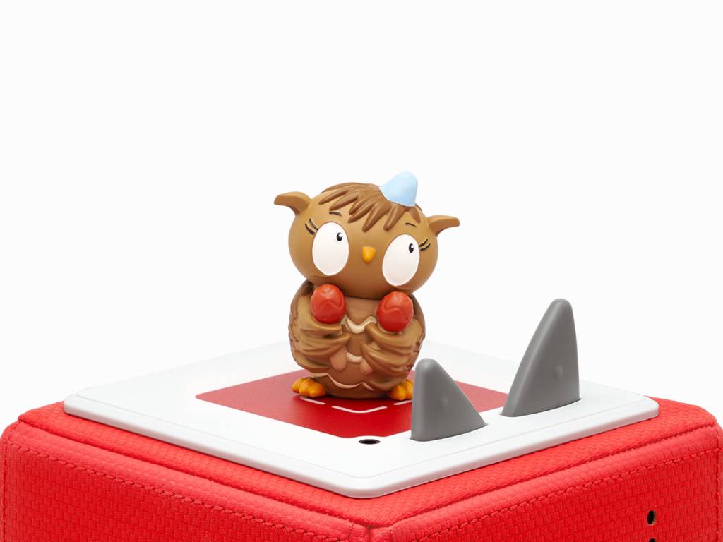 Kleine Eulenfigur mit roten Boxhandschuhen steht auf einer tablettenähnlichen Plattform oben auf einem roten Koffer.