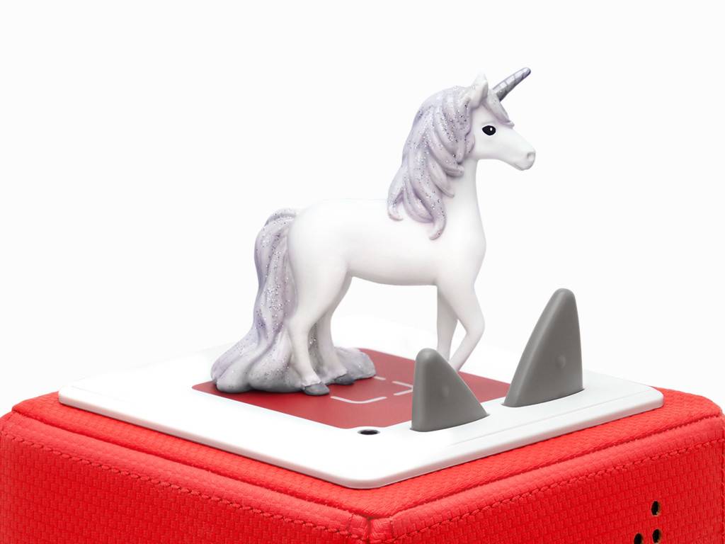 Weiße Einhorn-Figur auf einem kleinen Spielbrett, das auf einem roten Kissen liegt, mit zwei grauen dreieckigen Spielsteinen davor.