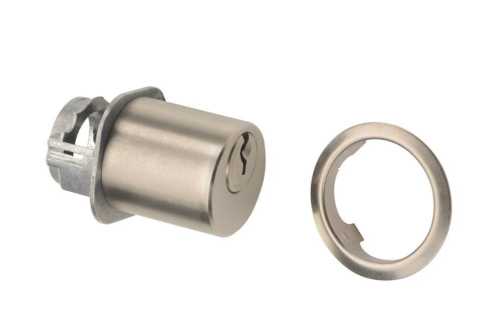 Ein zylindrischer Schlosskern mit einem Schlüsselloch neben einer runden, metallischen Abdeckplatte, beide aus einem schrägen Winkel betrachtet.