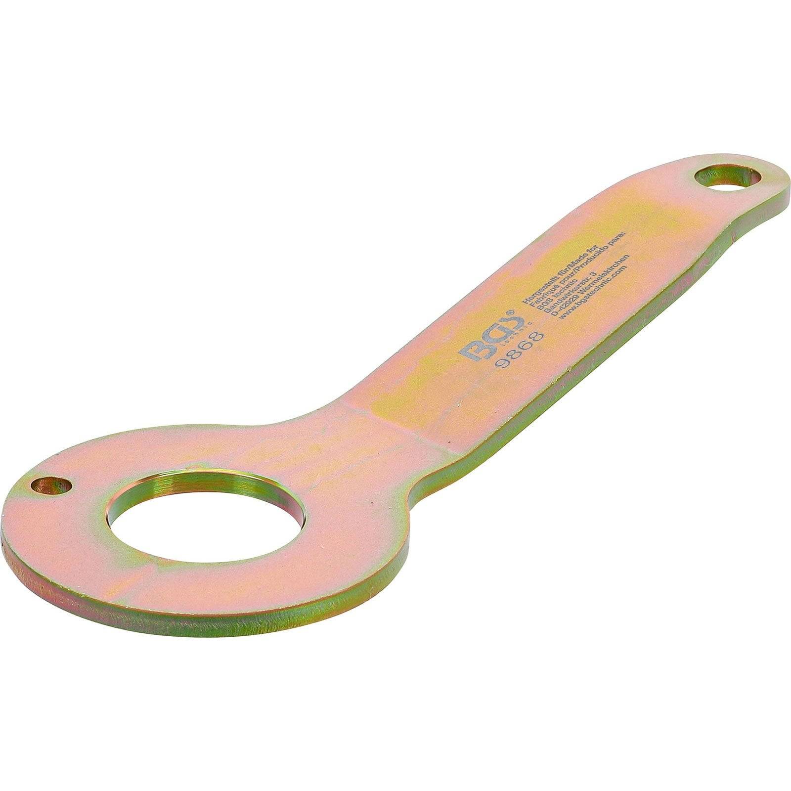 Ein Metallschraubenschlüssel mit flachem Griff und kreisförmigem Ende, der ein Loch zum Aufhängen aufweist. Das Metall hat einen gelblichen Farbton.