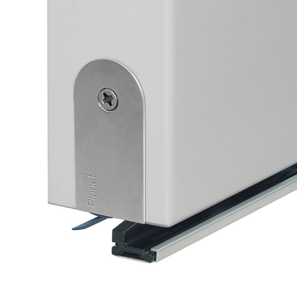 Eine silberfarbene Türunterdichtung, die an einer Türkante installiert ist, mit einer sichtbaren Befestigungsschraube, positioniert über einem schwarzen Bodenstreifen.