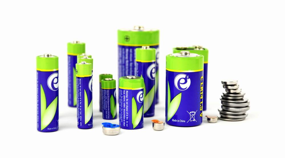 Sortierte grüne und blaue wiederaufladbare Batterien in verschiedenen Größen, mit einigen losen Knopfzellen auf weißem Hintergrund.