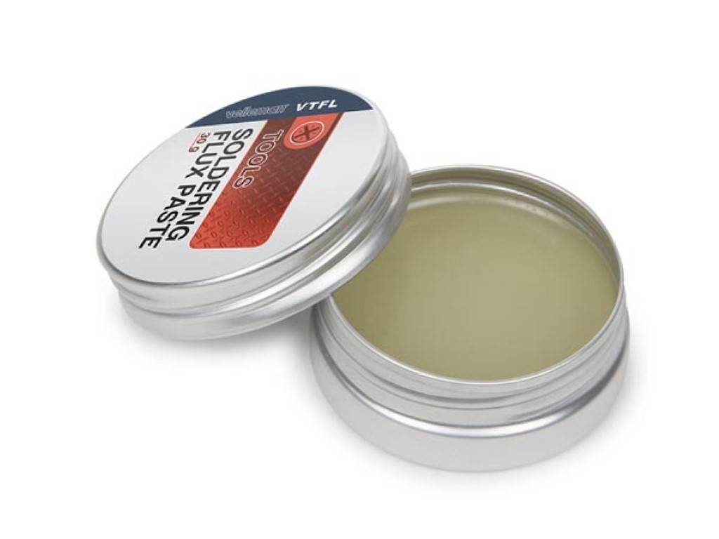 Offene Dose mit silbernem "Lötflussmittel-Paste"" mit beiger Paste im Inneren, Deckel daneben ruhend.