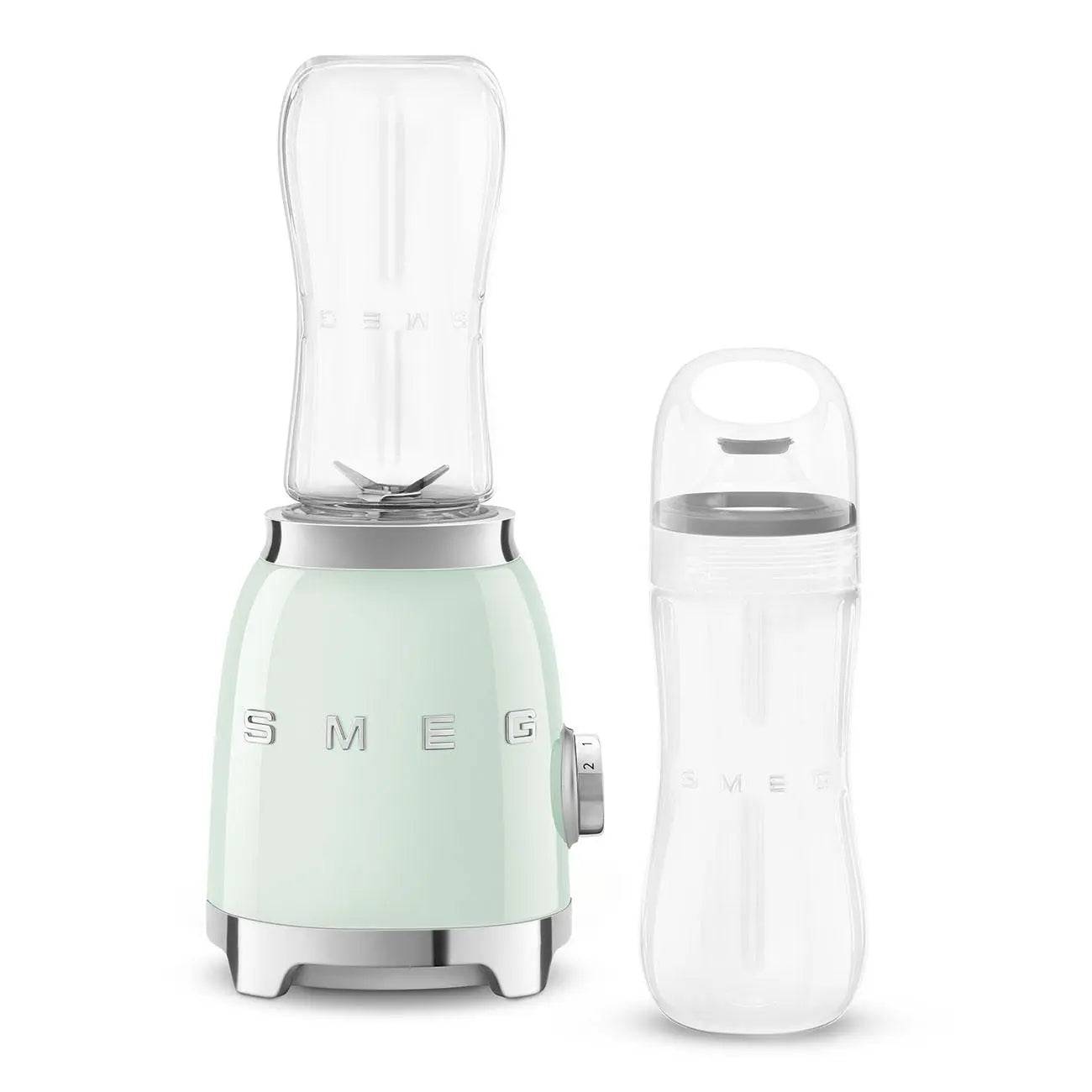 Minzgrüner SMEG-Mixer mit durchsichtigem Mixbehälter neben einer passenden durchsichtigen Reiseflasche auf weißem Hintergrund.