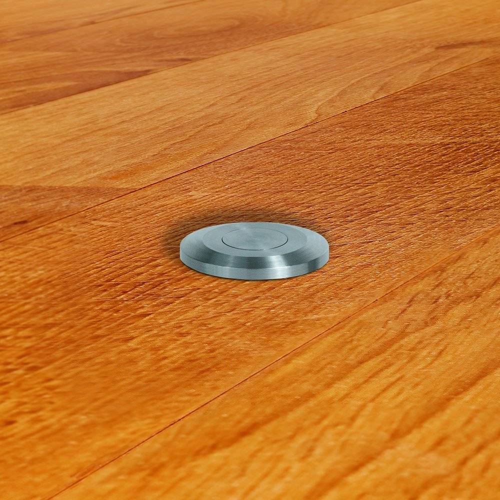 Eine runde Metallsteckdose ist in einen polierten Holzboden integriert, fügt sich nahtlos ein und bietet diskrete elektrische Zugriffsmöglichkeiten.