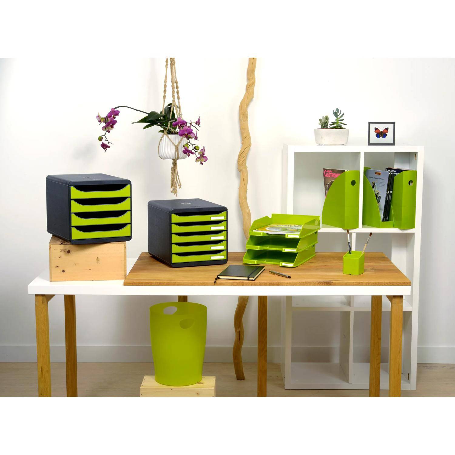 Moderner Arbeitsbereich mit schwarzen und limegrünen Aufbewahrungsorganizern, Ordnern, Schreibtischaccessoires und einer kleinen Pflanze auf einem weißen Tisch vor einer minimalistischen Wand.