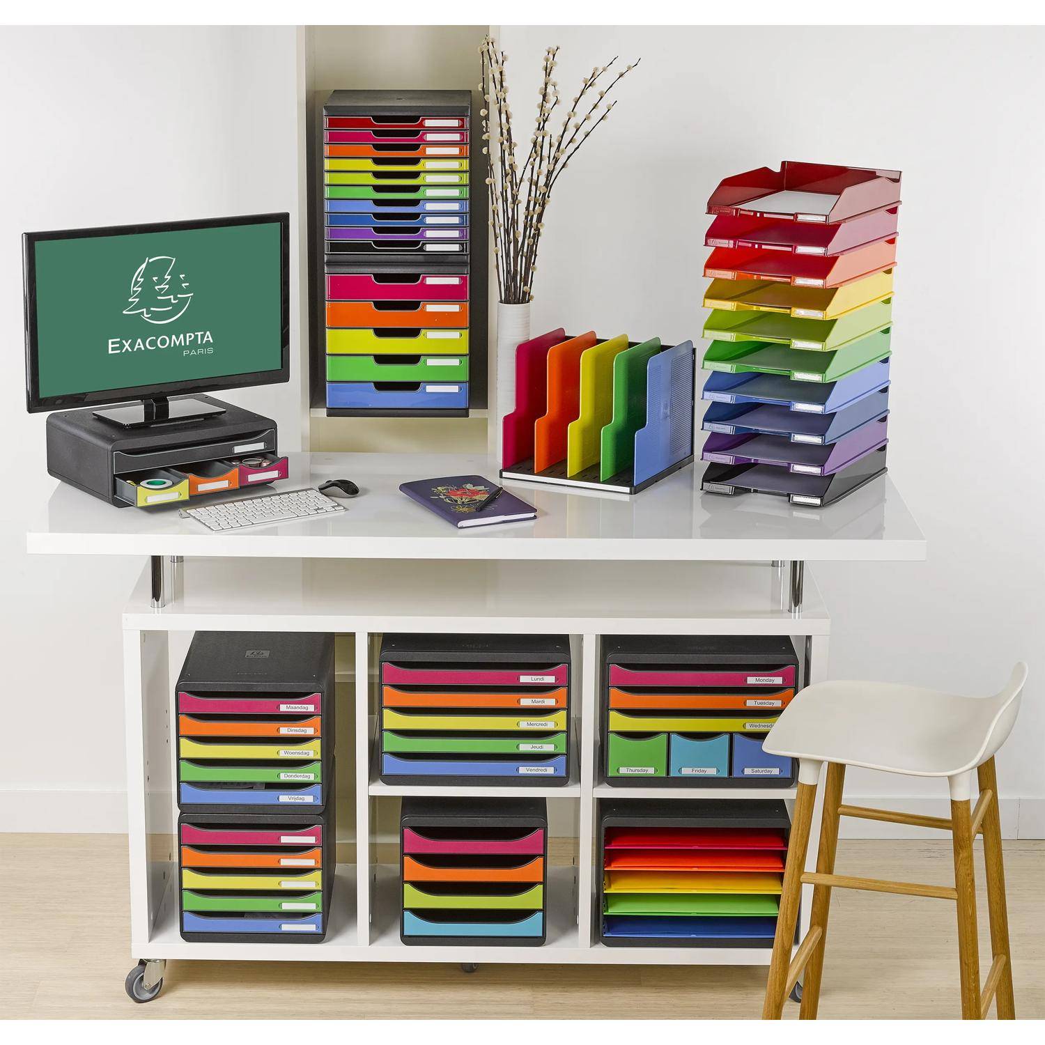 Organisierter Büroarbeitsplatz mit einem Computer, einer Tastatur und mehreren farbenfrohen Dokumentablagen und Aktenholdtern, die auf einem weißen Schreibtisch und einer Regalanlage angeordnet sind.