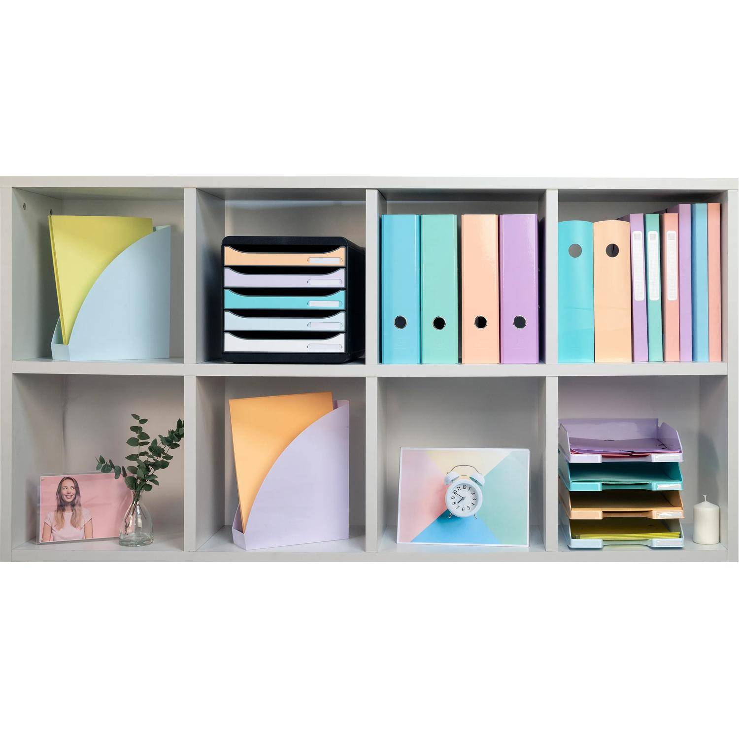 Ein weißes Cubby-Regal, organisiert mit pastellfarbenen Ordnern, Aktenmappen, Notizbüchern, einer kleinen Pflanze, einem Foto und einem Wecker.