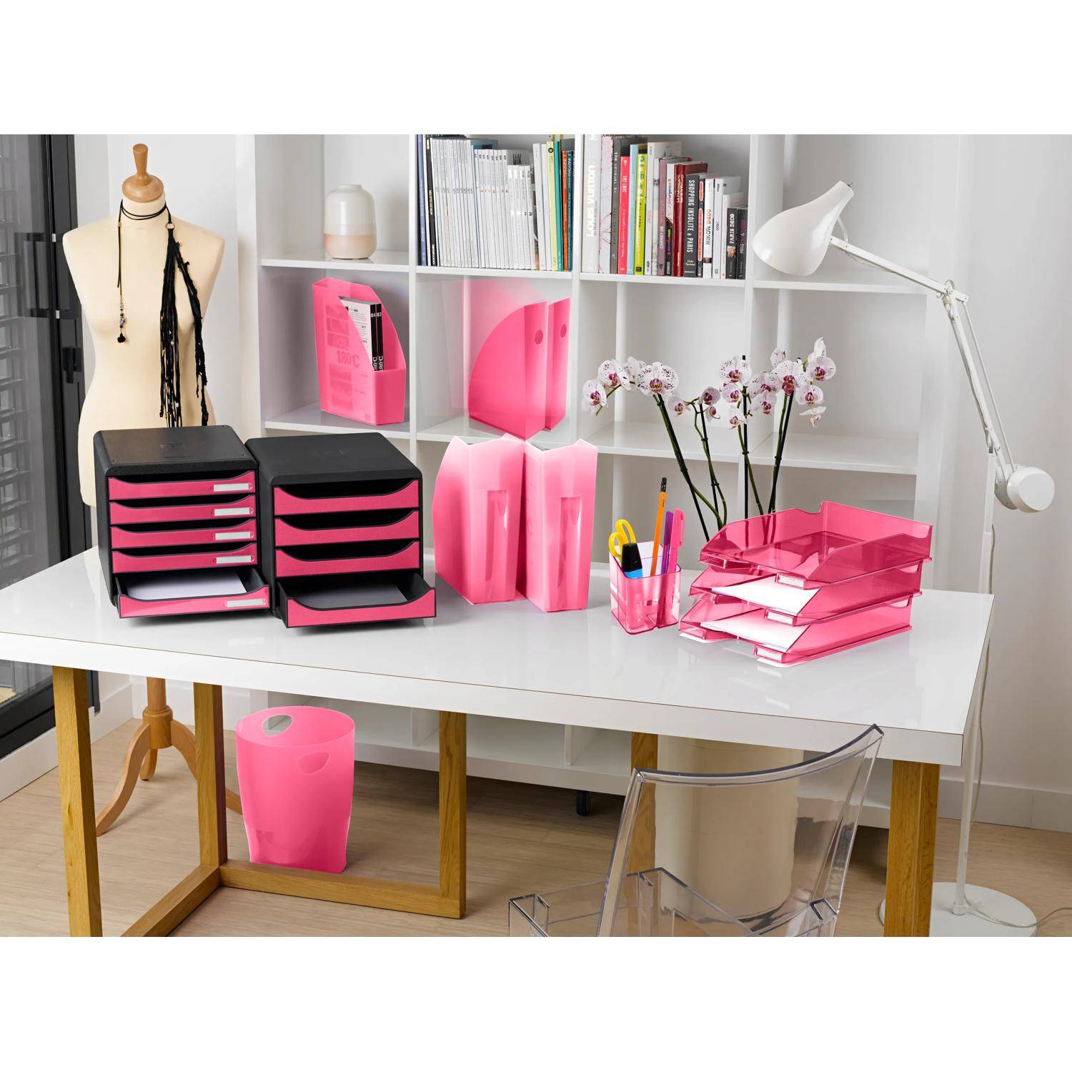 Ein stilvolles Bürotischset mit rosa Organizer, Ordnern, Büchern, einer Schneiderpuppe und einer weißen Lampe neben einem Regal.