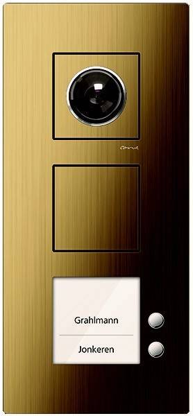 Goldfarben elektrisches Schaltertableau mit zwei quadratischen Tasten und einem runden Drehknopf oder einer Linse oben, vor einer reflektierenden Oberfläche.