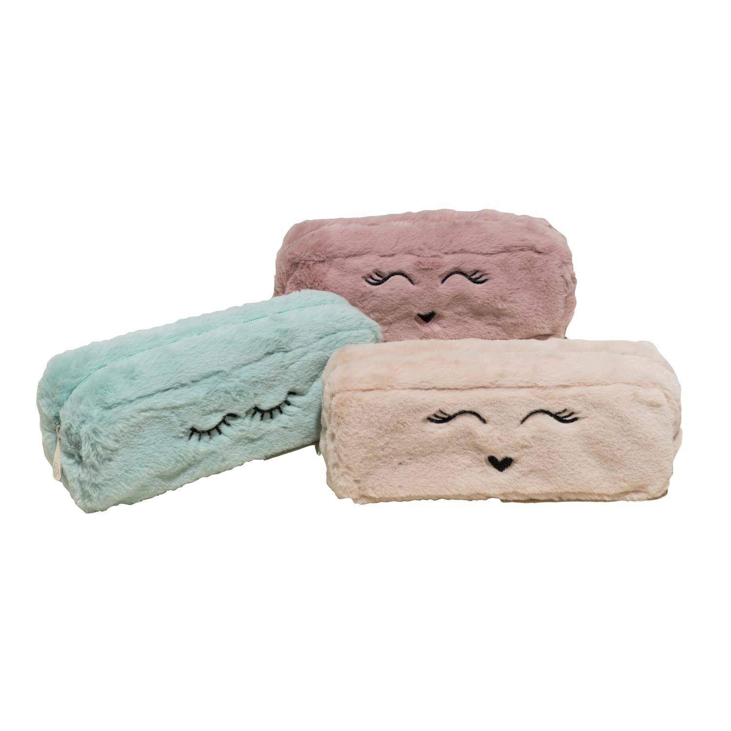 Drei plüschige rechteckige Kissen in Pastellrosa, Minzgrün und Beige, jeweils mit einem lächelnden gestickten Gesicht auf weißem Hintergrund.