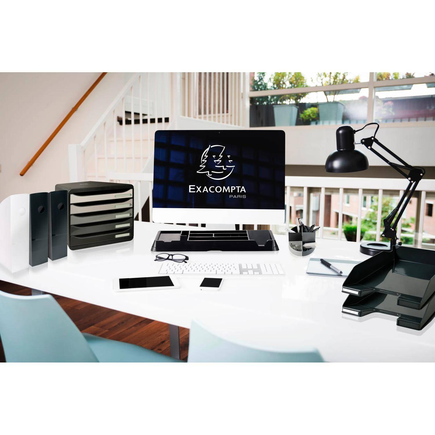 Moderner Home-Office-Schreibtisch mit iMac, auf dem "EXACOMPTA PARIS"" angezeigt wird, Papierablage, Lampe, Tablet und Schreibwaren neben einem hellen Fenster.