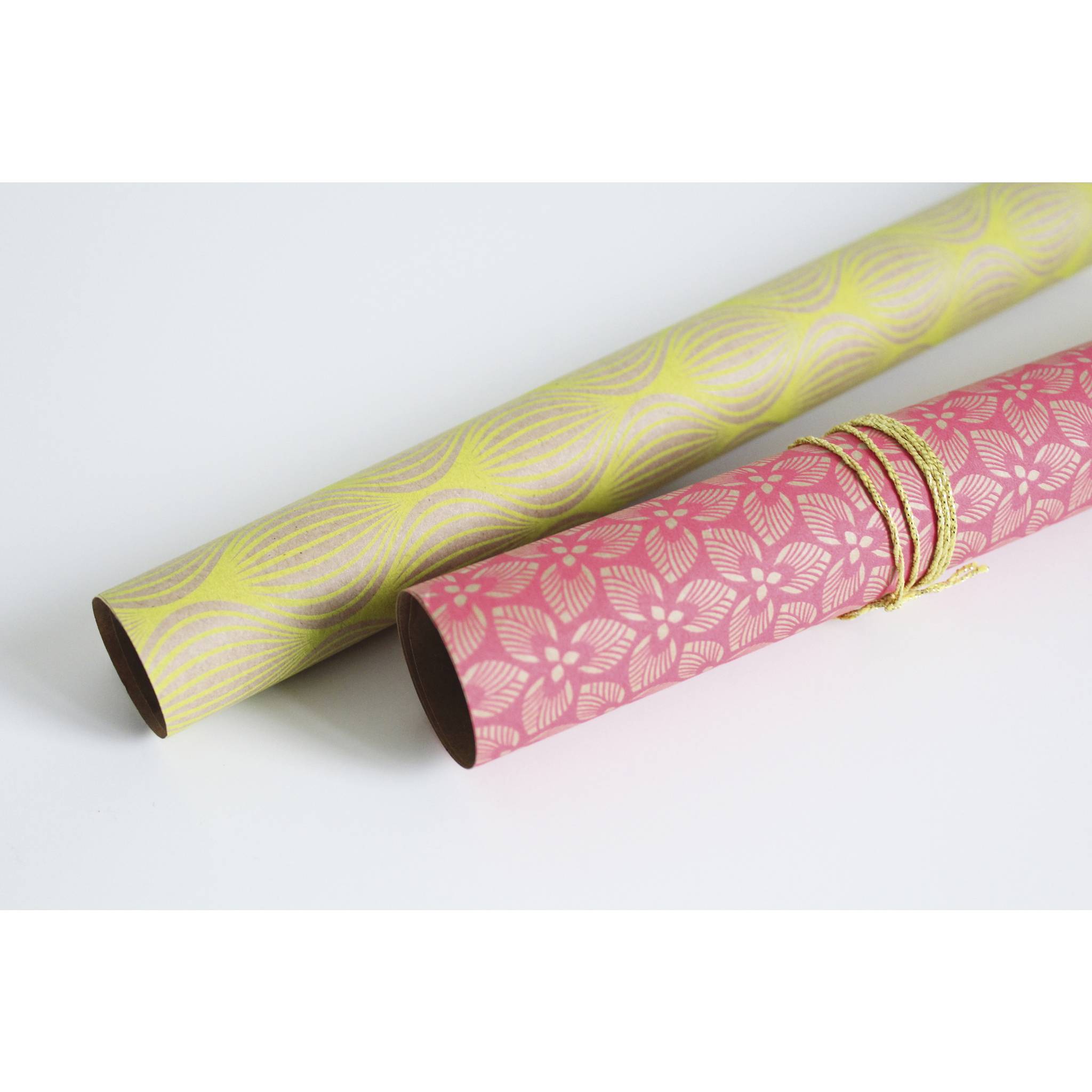 Zwei dekorative Geschenkpapierrollen, eine gelbgrün und eine rosa mit Blütenmustern, mit goldenem Garn auf weißem Hintergrund gebunden.