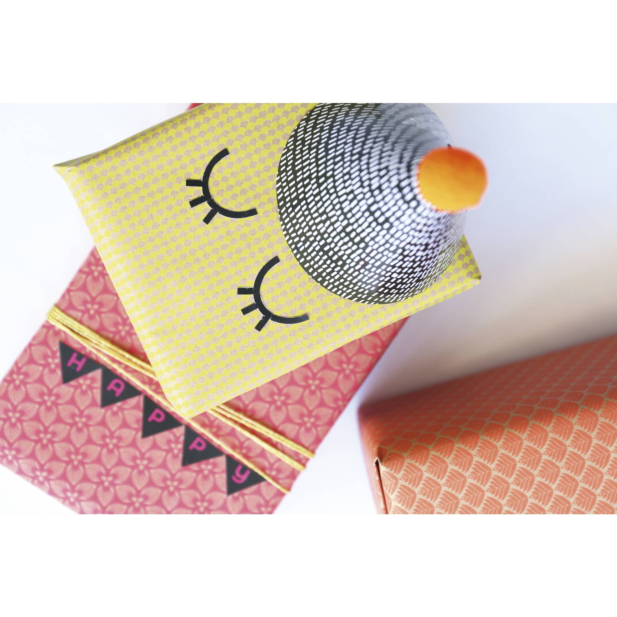 Verzierte handgefertigte Geschenkboxen in Form einer Katze mit geschlossenen Augen und einem silbernen Partyhut, neben einer orangefarbenen gemusterten Box.