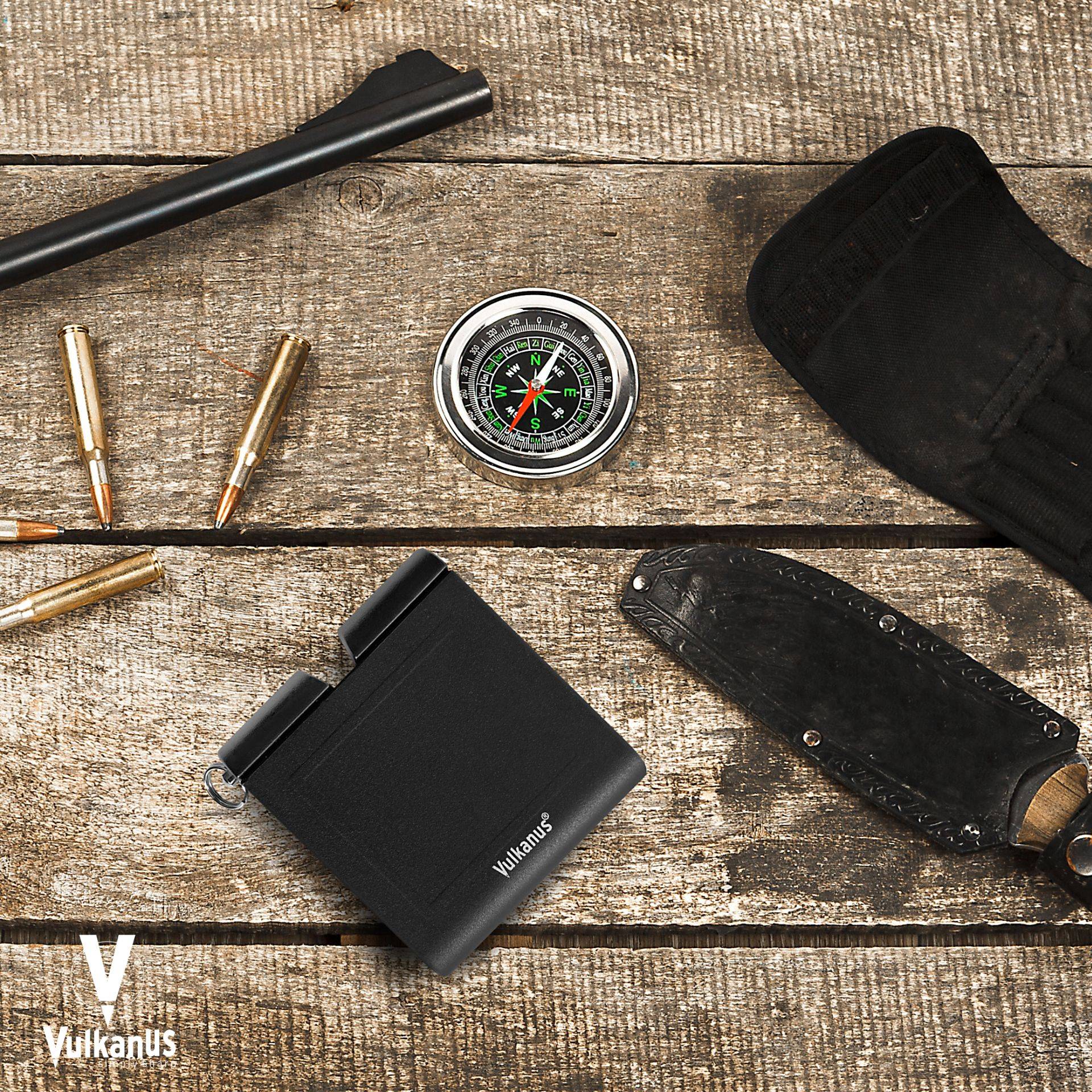 Ein kleines schwarzes Überlebensset mit einem Messer, einem Kompass und Munition ist auf einer rustikalen Holzoberfläche angeordnet.
