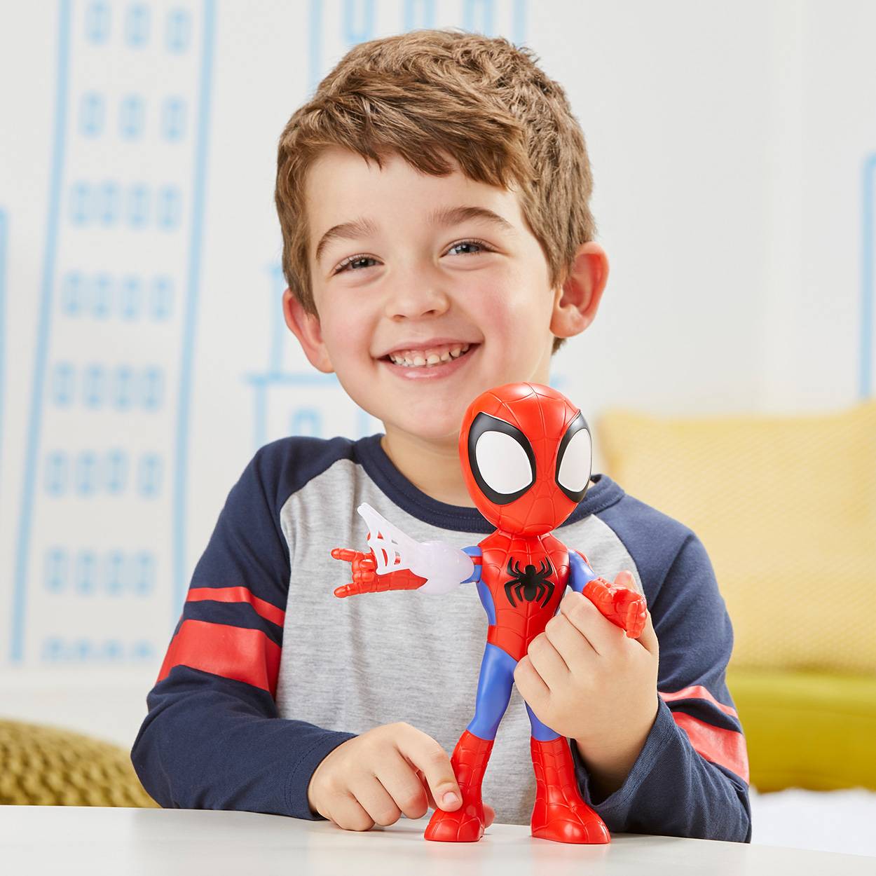 Lächelnder junger Junge, der eine Spider-Man-Actionfigur an einem Tisch in einem Innenraum hält.