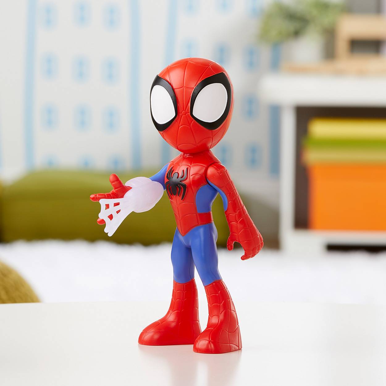 Spider-Man-Actionfigur, die auf einer weißen Oberfläche steht und ein kleines weißes Zubehörteil hält, mit unscharfem Hintergrund eines Innenraums.
