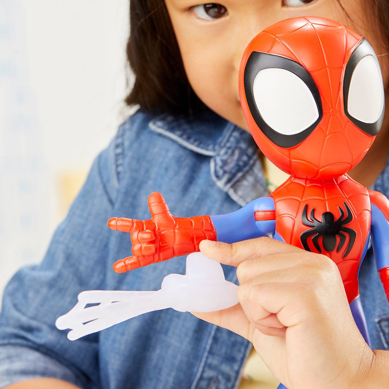 Kind, das eine Spider-Man-Spielfigur nah an der Kamera hält, trägt ein Jeanshemd in einer hellen Innenumgebung.