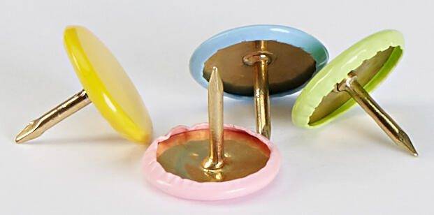 Vier farbenfrohe Goldreißzwecken, die auf ihrer Seite liegen: gelb, rosa, blau und grün.