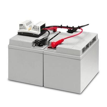 Eine Notstromanlage mit zwei großen grauen Batterien, die über rote und schwarze Kabel mit einem Stromgerät auf der Oberseite verbunden sind und für die Stromversorgung im Notfall verwendet werden.