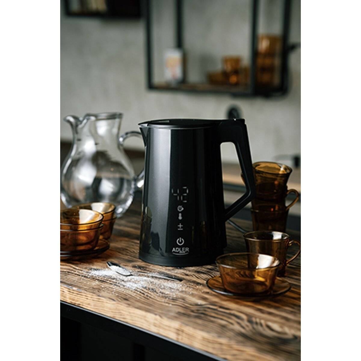 Ein schwarzer elektrischer Wasserkocher auf einem rustikalen Holztisch, umgeben von bernsteinfarbenen Glastassen und einer Glaskanne, das eine gemütliche Küchenatmosphäre vermittelt.