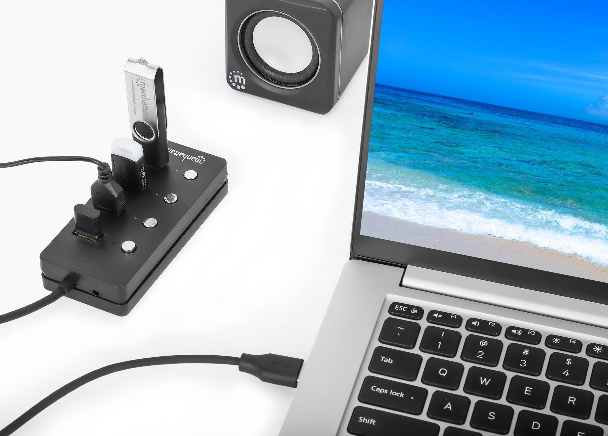 Laptop, das mit einem USB-Docking-Hub verbunden ist, mit angeschlossenen Laufwerken und Audiogeräten auf einem weißen Schreibtisch.