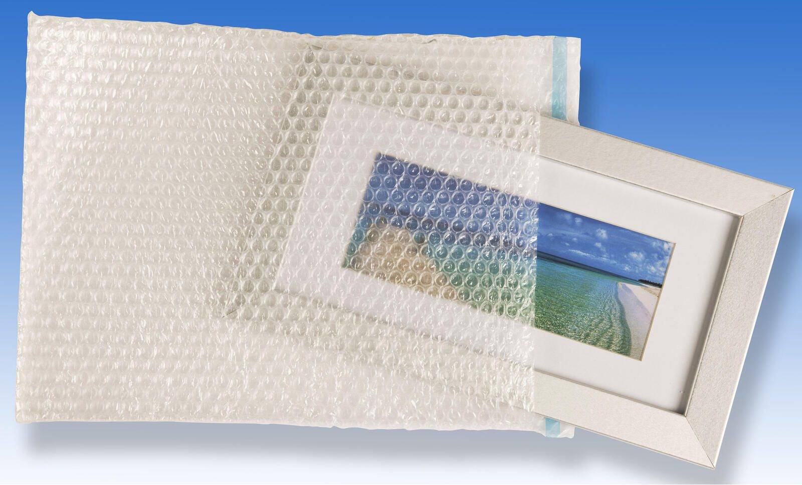 Ein gerahmtes Strandlandschafts-Foto, teilweise in Luftpolsterfolie eingewickelt, vor einem einfarbig blauen Hintergrund.
