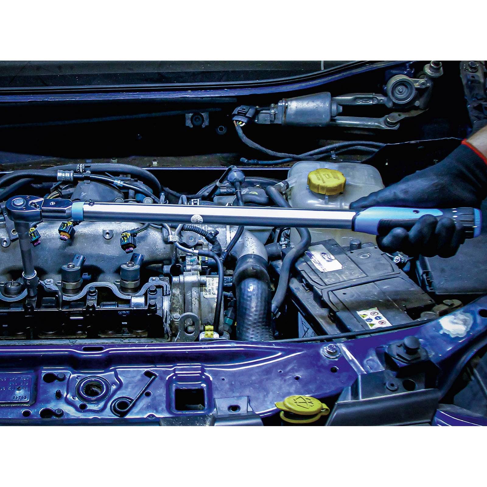 Eine Person verwendet einen Drehmomentschlüssel, um Teile im Motorraum eines Autos einzustellen, was Fahrzeugwartung oder Reparaturarbeiten veranschaulicht.