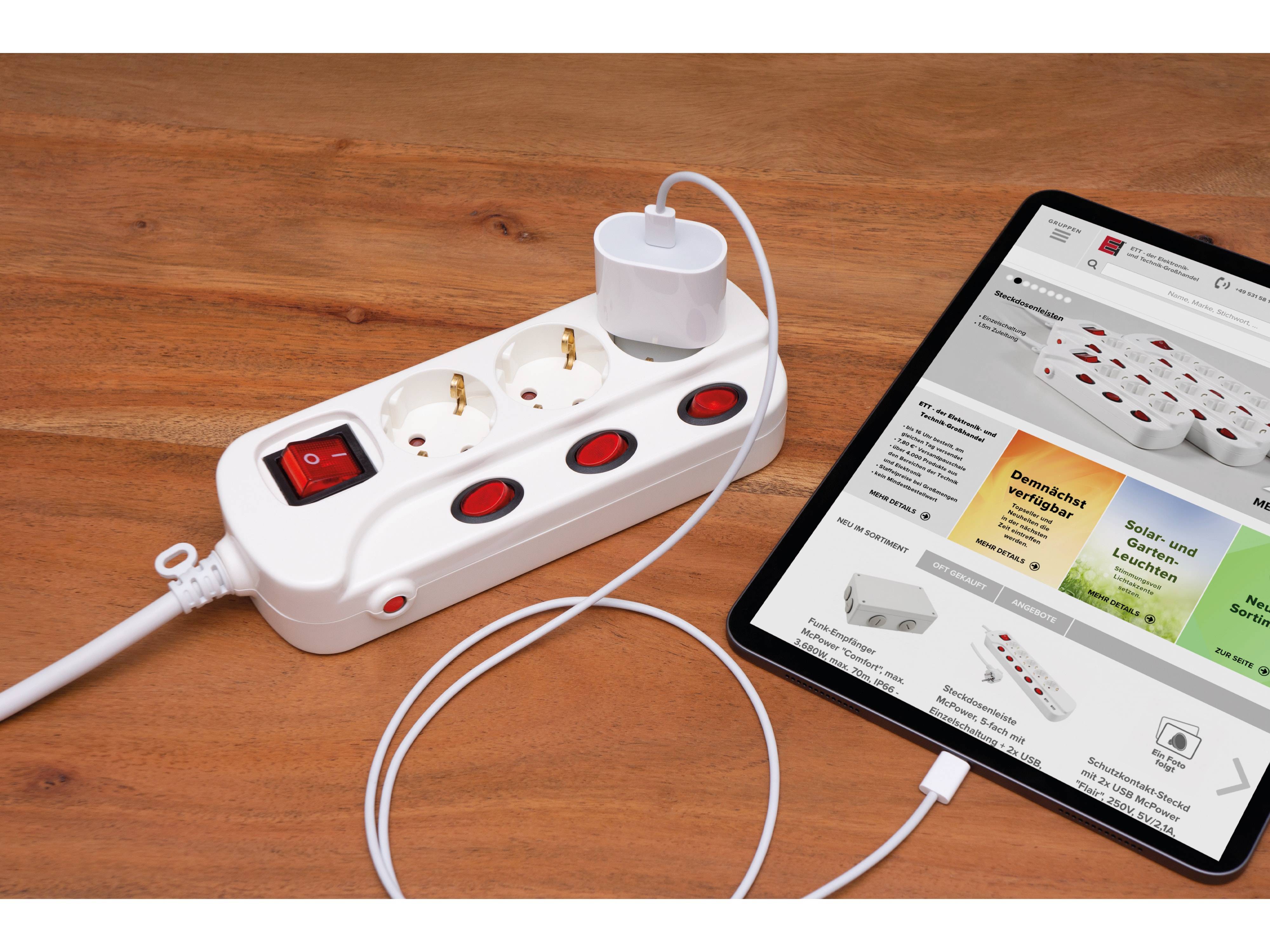 Eine Steckerleiste mit angeschlossenen Geräten neben einem Tablet, auf dem eine Online-Shopping-Seite mit Steckerleisten und verwandten Produkten angezeigt wird.