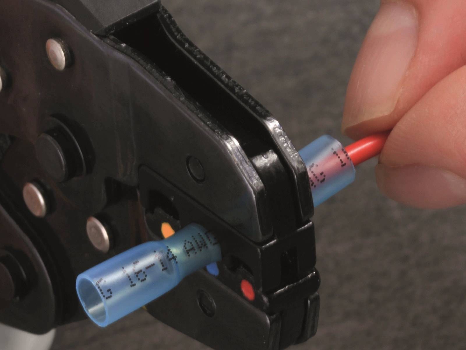 Crimpwerkzeug, das einen blauen Stecker auf ein rotes Kabel presst und eine sichere elektrische Verbindung zeigt.