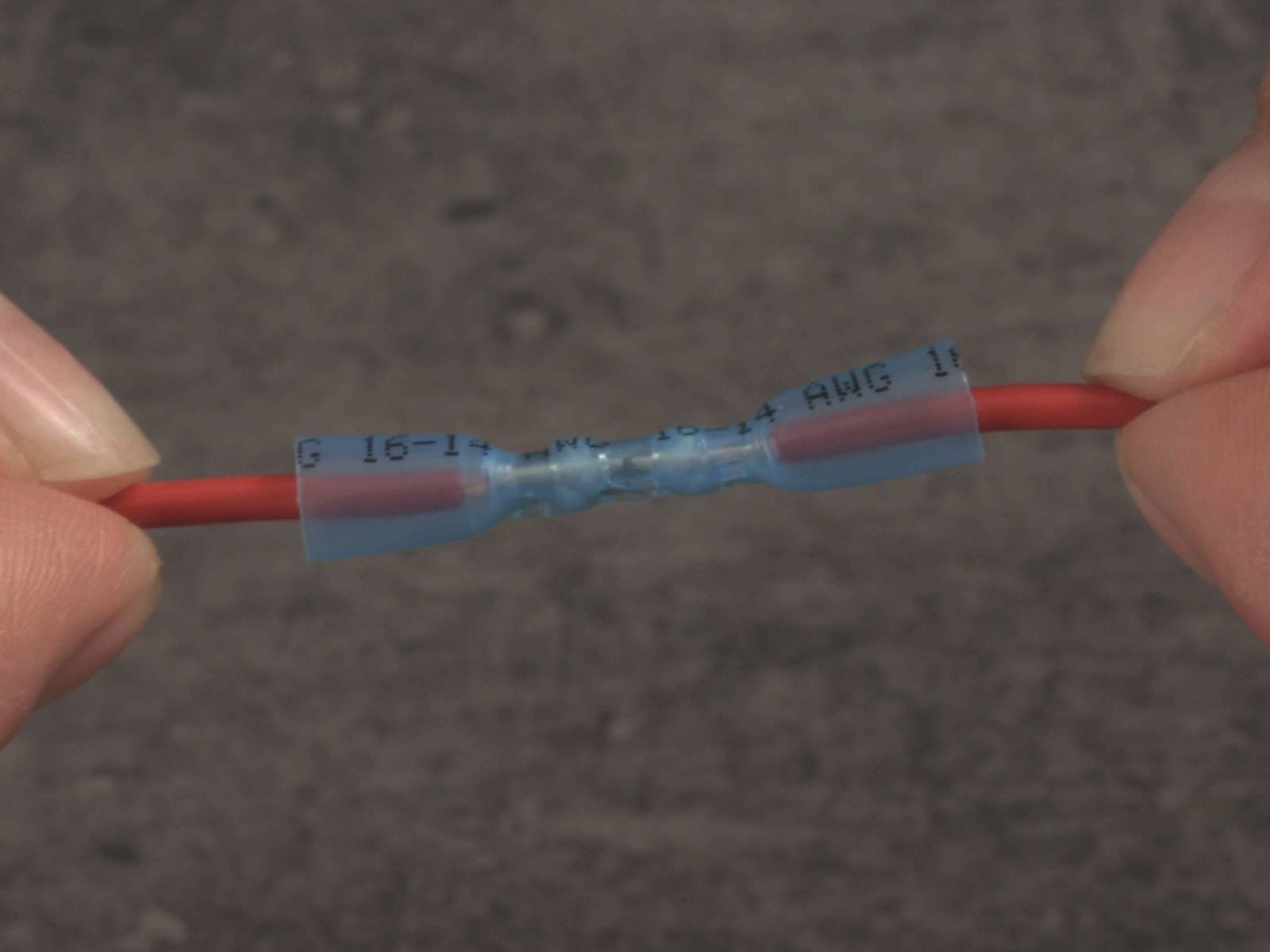 Ein Paar roter Elektrokabel, die durch einen blauen isolierten Verbinder verbunden sind, mit Spezifikationen gekennzeichnet und zeigend eine sichere Verbindungsstelle.